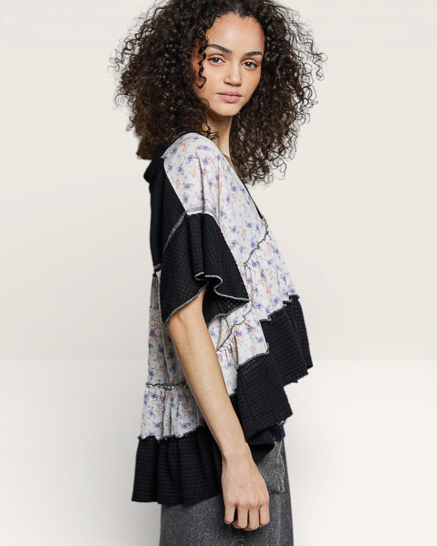 Woman wearing a floral top with black sleeves and trim on a plain background
