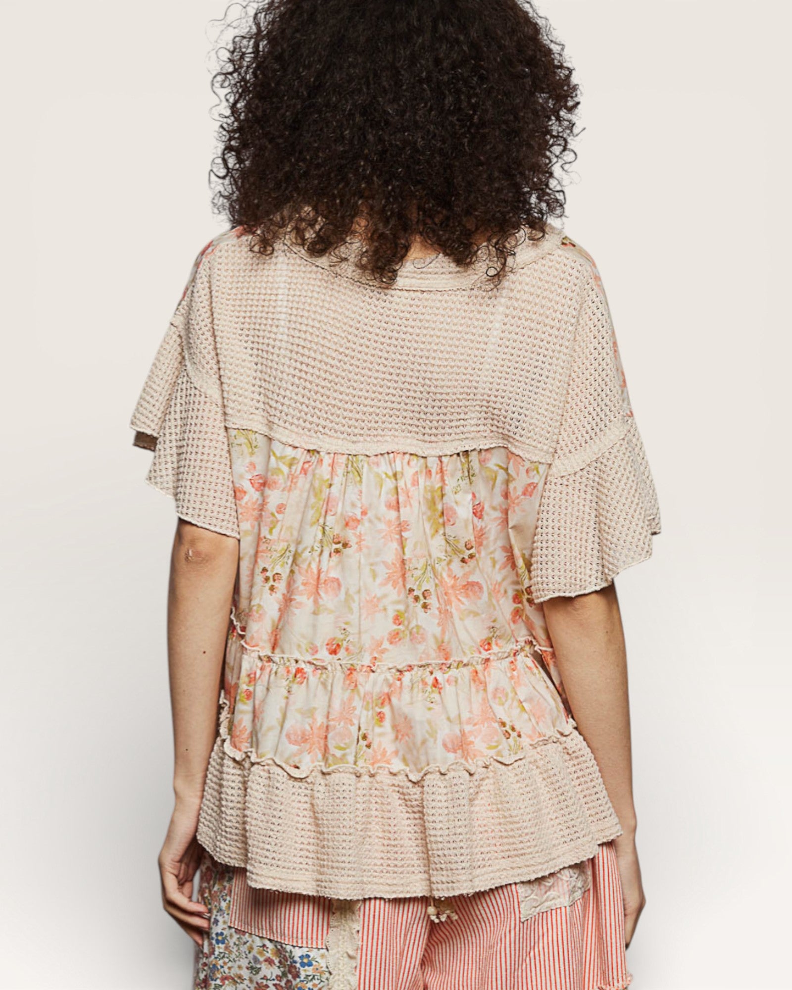 Woman wearing a layered dress with floral top and striped skirt on a plain background