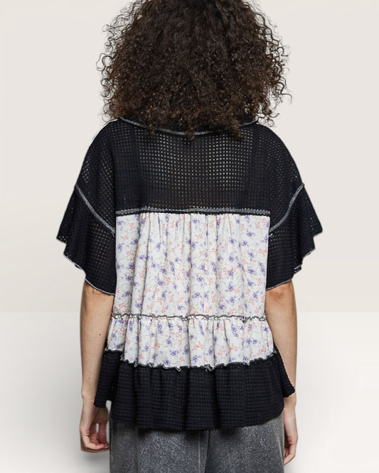 Person wearing a black and floral layered top on a plain background