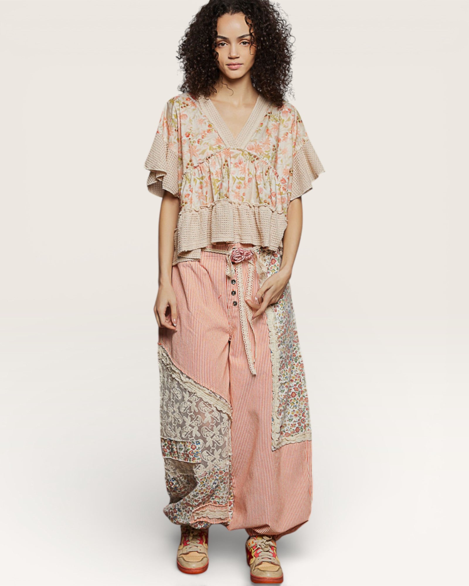 Woman wearing a floral top and pink pants with a patterned scarf on a white background