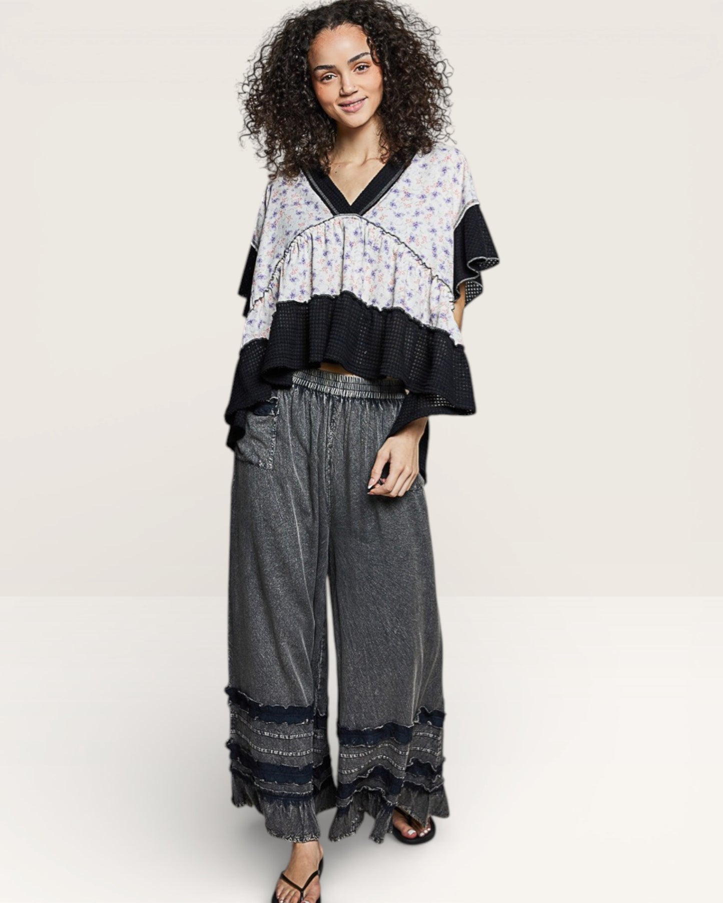 Woman wearing a floral top and wide-leg pants on a white background