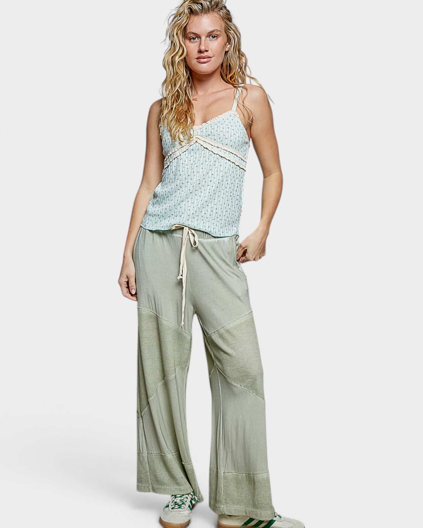 Woman wearing a light green sleeveless top and wide-leg pants on a white background