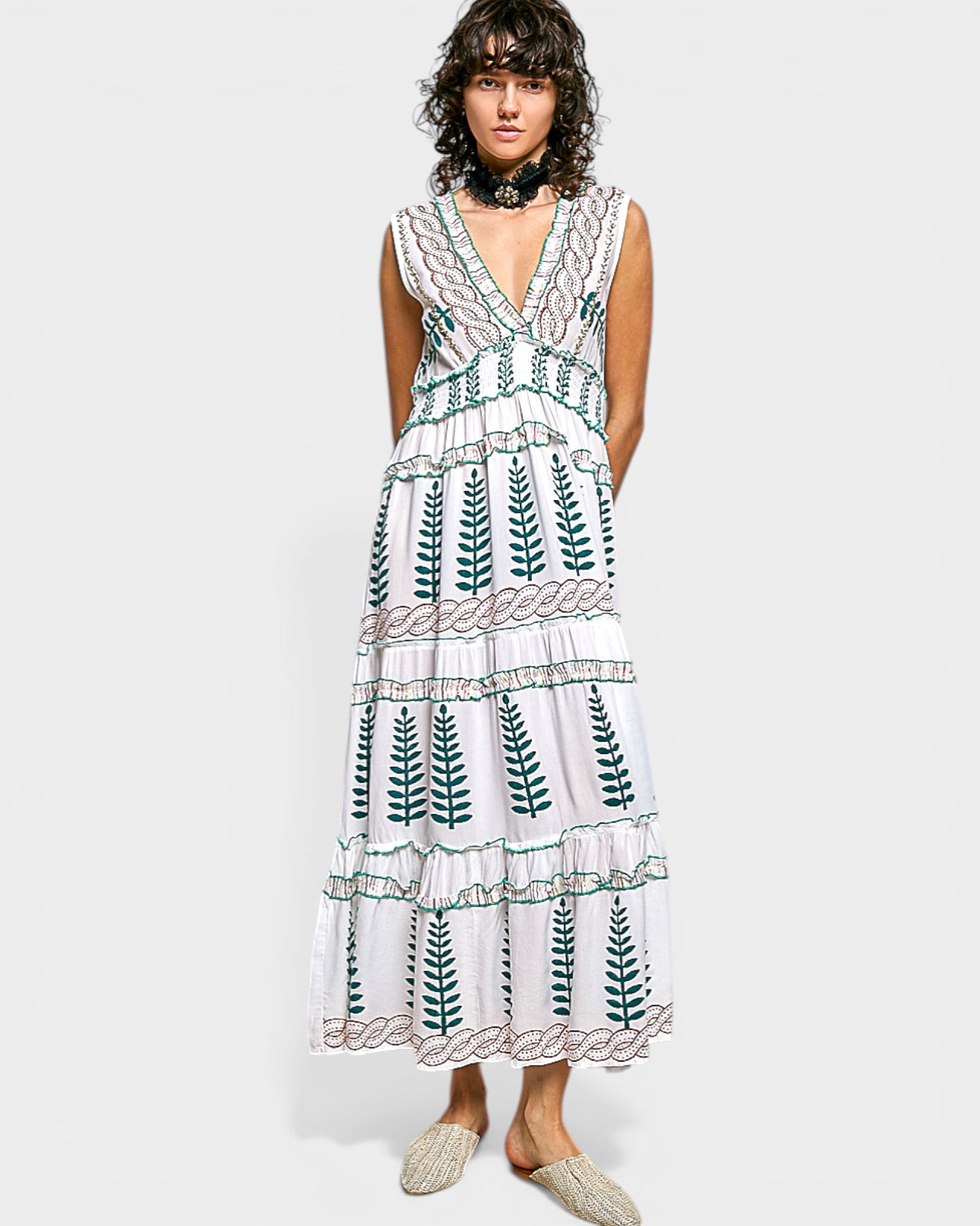 Woman wearing a white dress with green leaf patterns on a plain background
