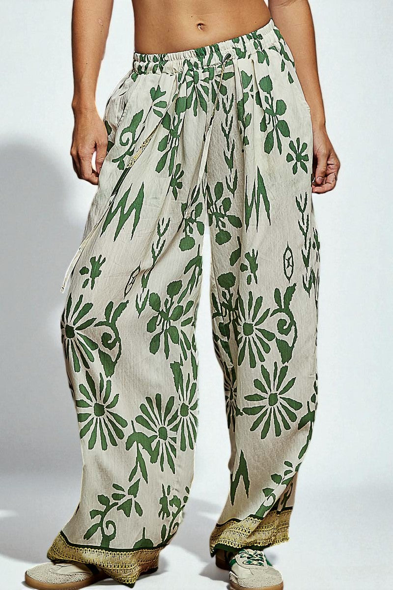 Beige pants with green floral patterns worn by a person on a white background