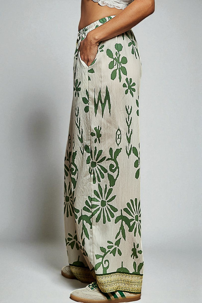 Person wearing a long, patterned skirt with green floral design on a plain background