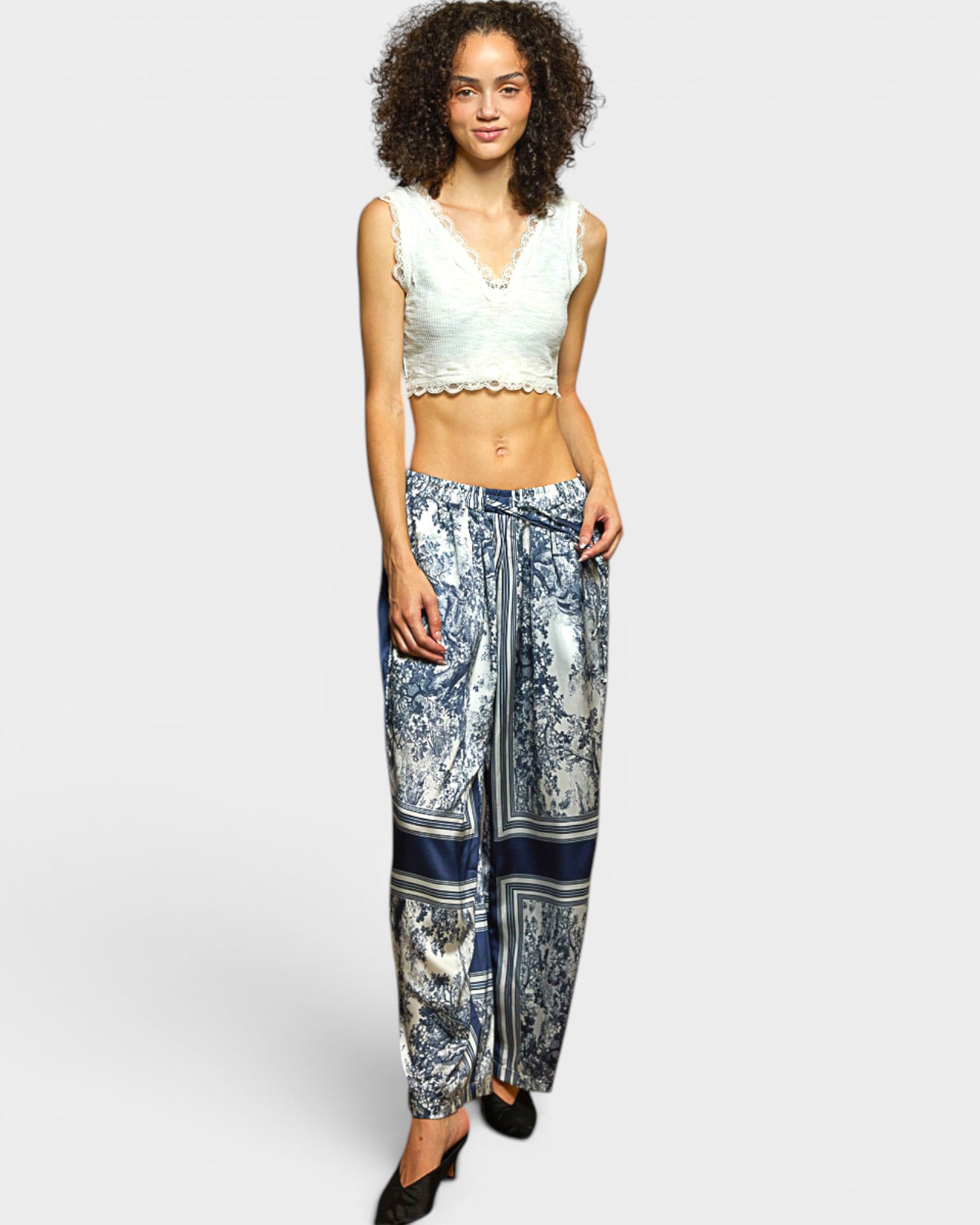 Woman wearing a white sleeveless top and patterned pants on a white background