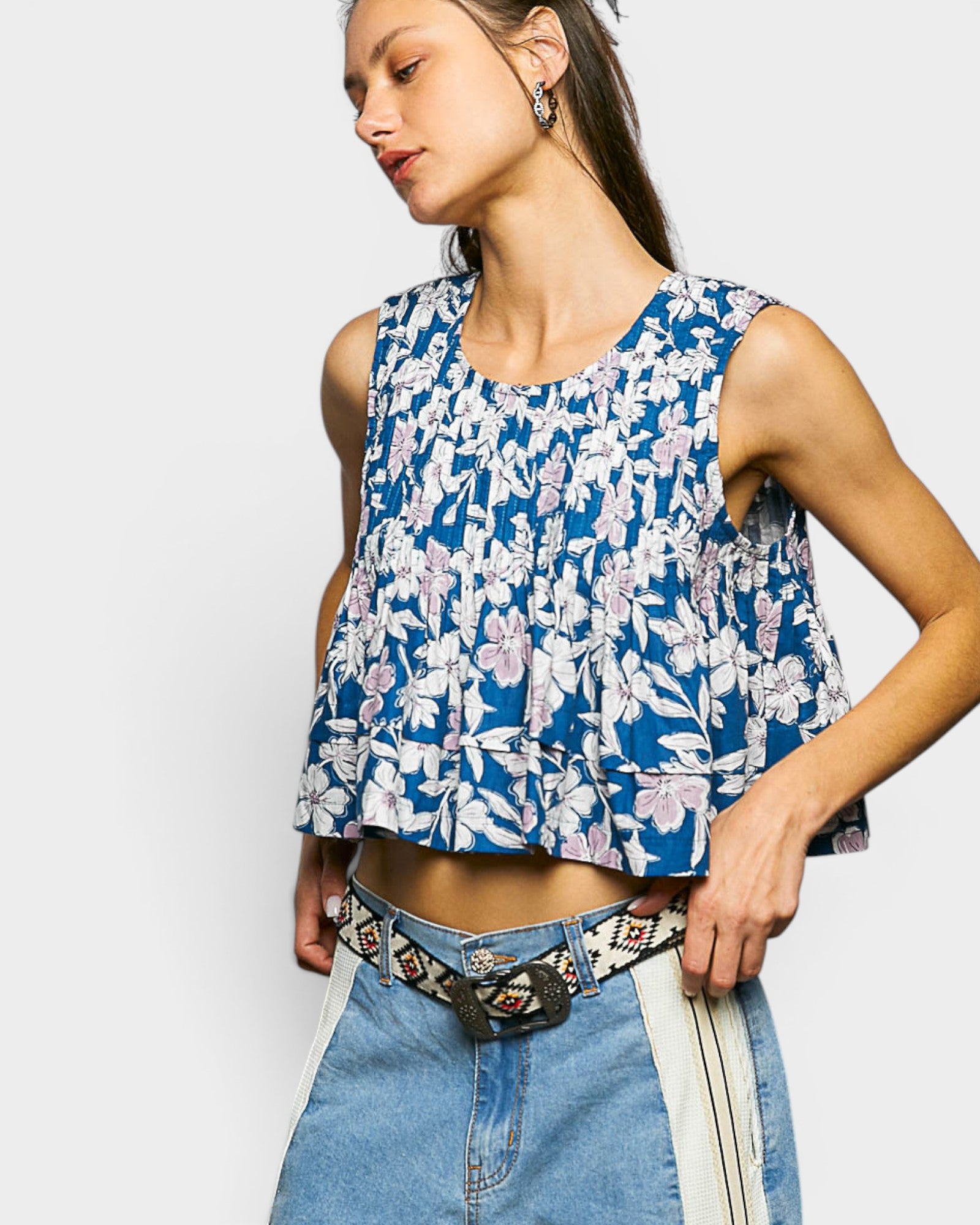 Woman wearing a blue floral sleeveless top and denim jeans on a white background