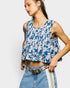 Woman wearing a blue floral sleeveless top and denim jeans on a white background