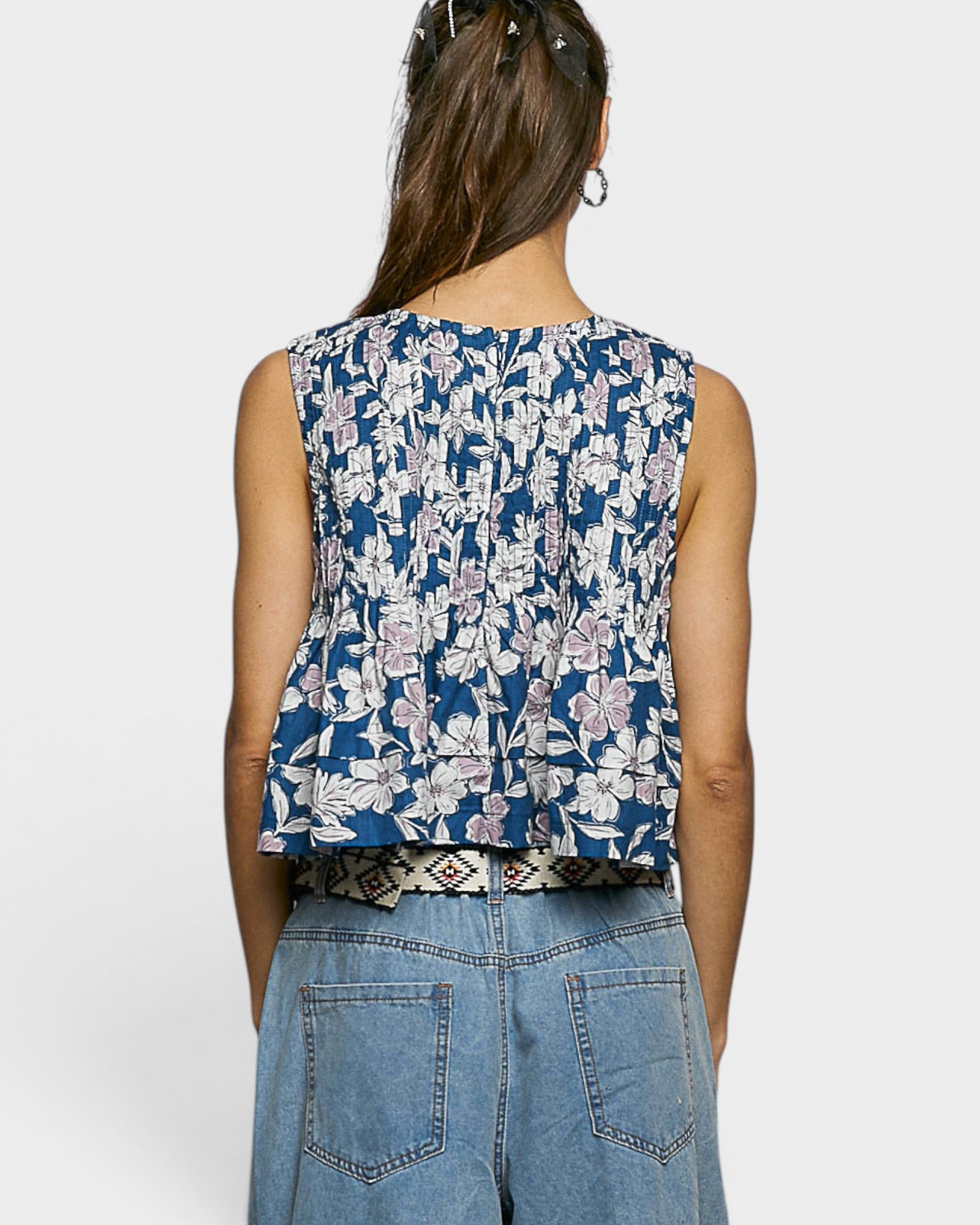 Person wearing a sleeveless floral top and blue jeans on a white background