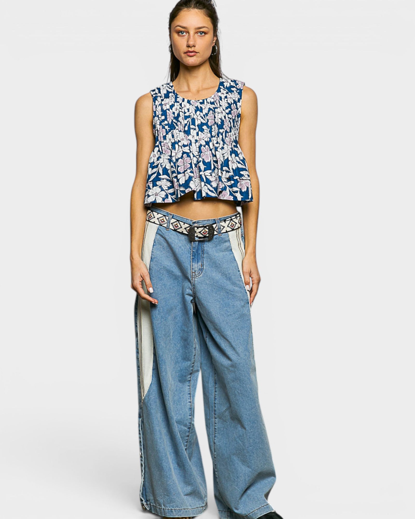 Woman wearing a blue floral sleeveless top and wide-leg jeans on a white background