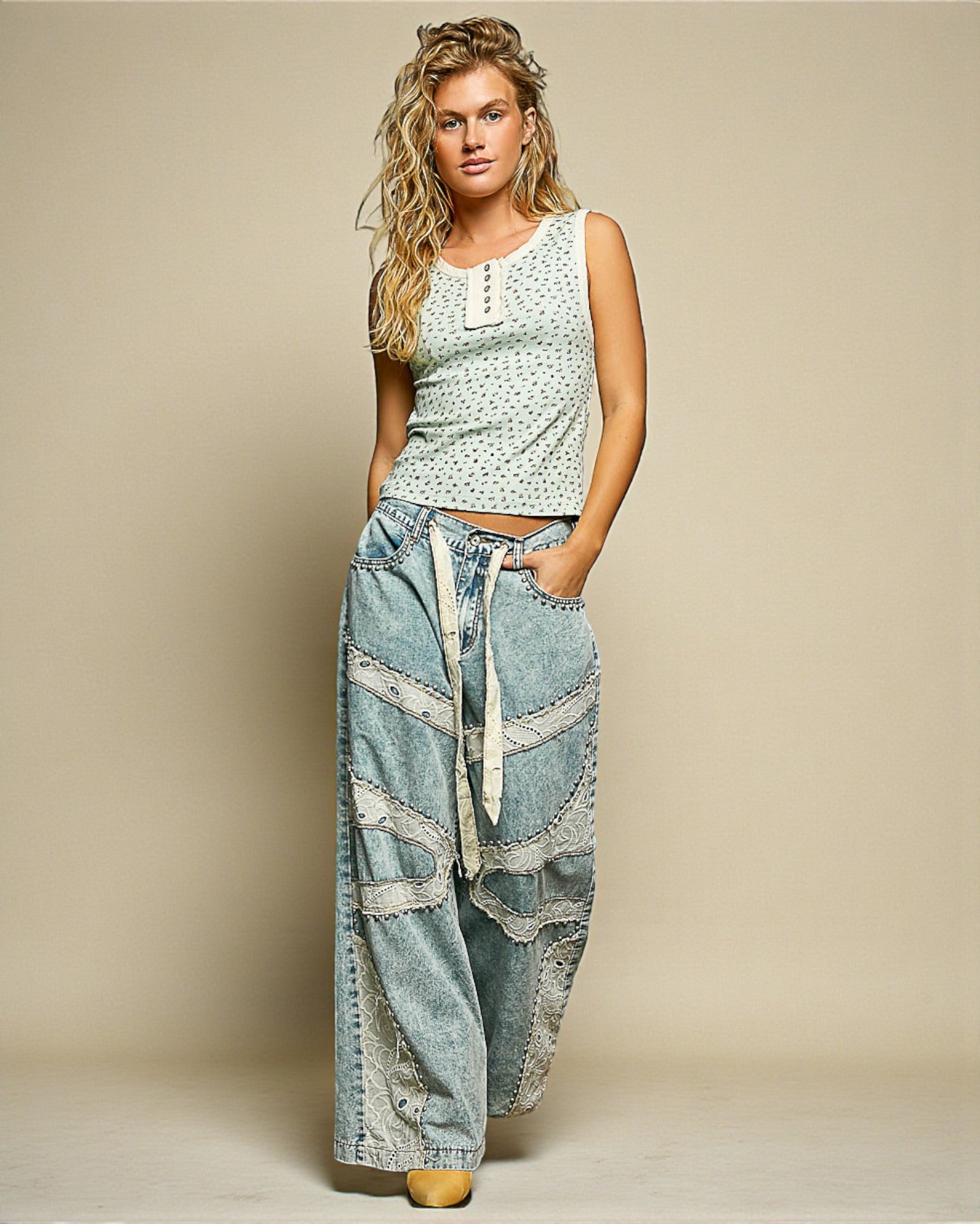 Woman wearing a sleeveless top and wide-leg jeans against a beige background