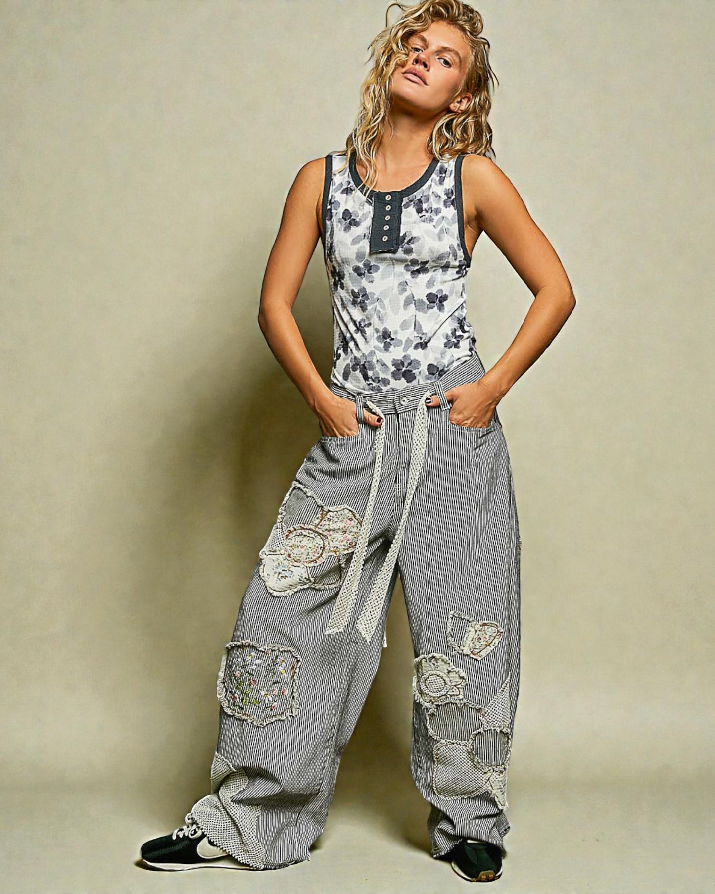 Woman wearing a floral tank top and gray pants with lace details on a beige background