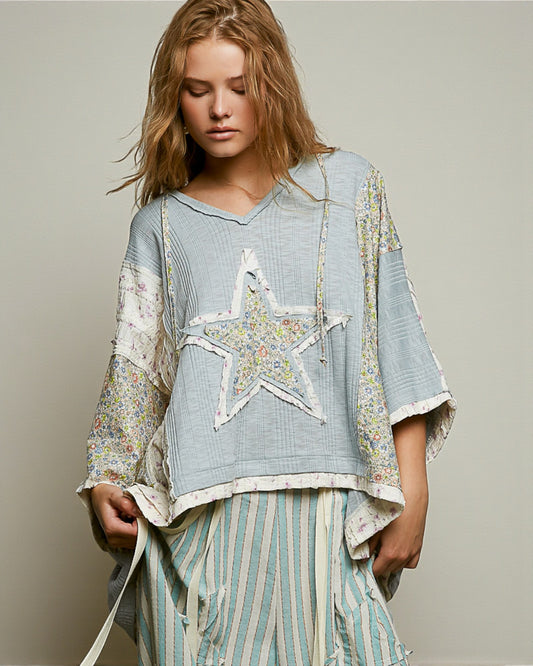 Woman wearing a light blue top with a star design and striped pants on a neutral background