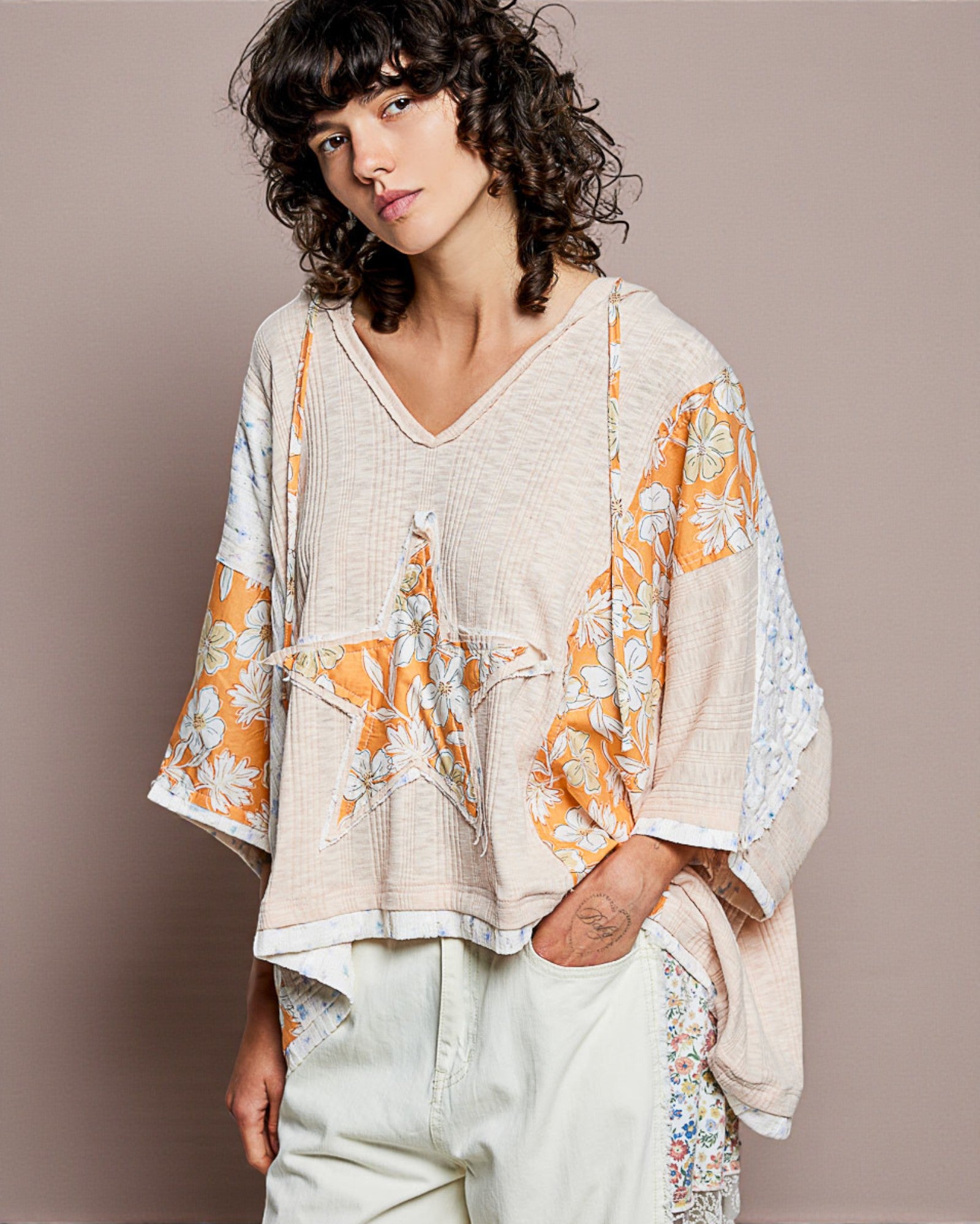 Woman wearing a beige and orange floral blouse with a plain background