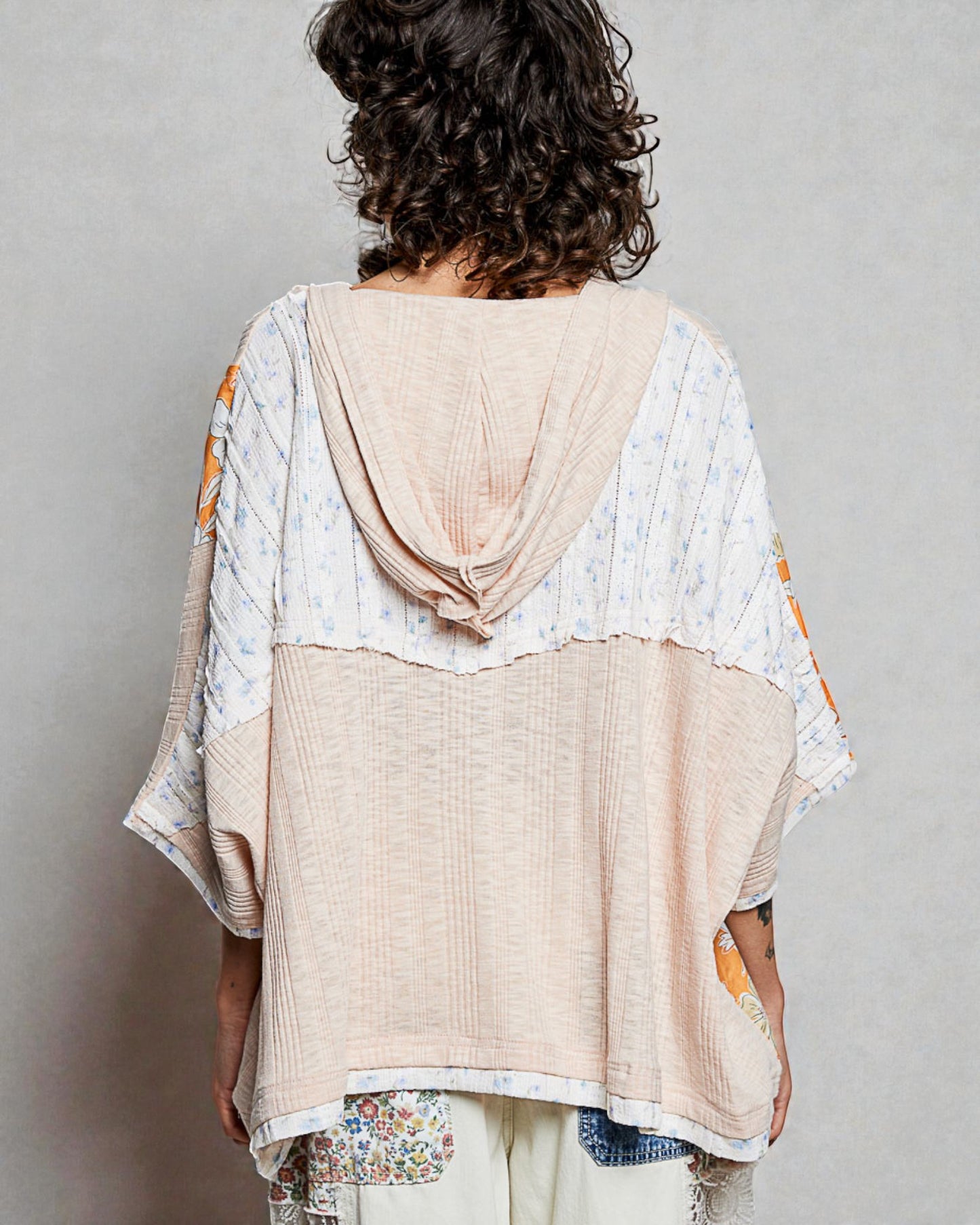 Person wearing a beige and patterned top with a plain background