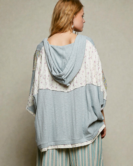 Woman wearing a layered outfit with a light blue top and patterned pants against a neutral background