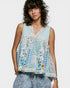 Woman wearing a sleeveless, floral-patterned top with a light blue background