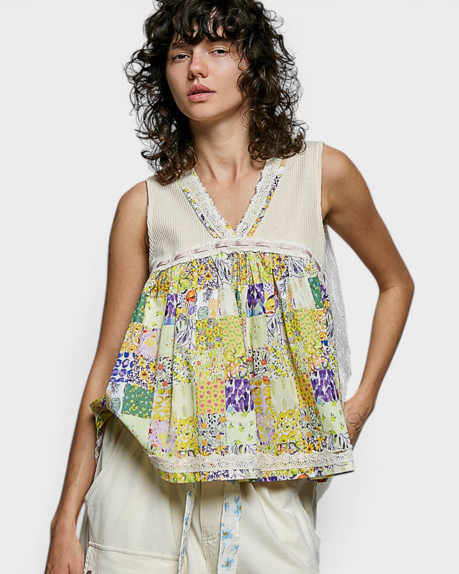 Woman wearing a sleeveless, patchwork top with a plain background