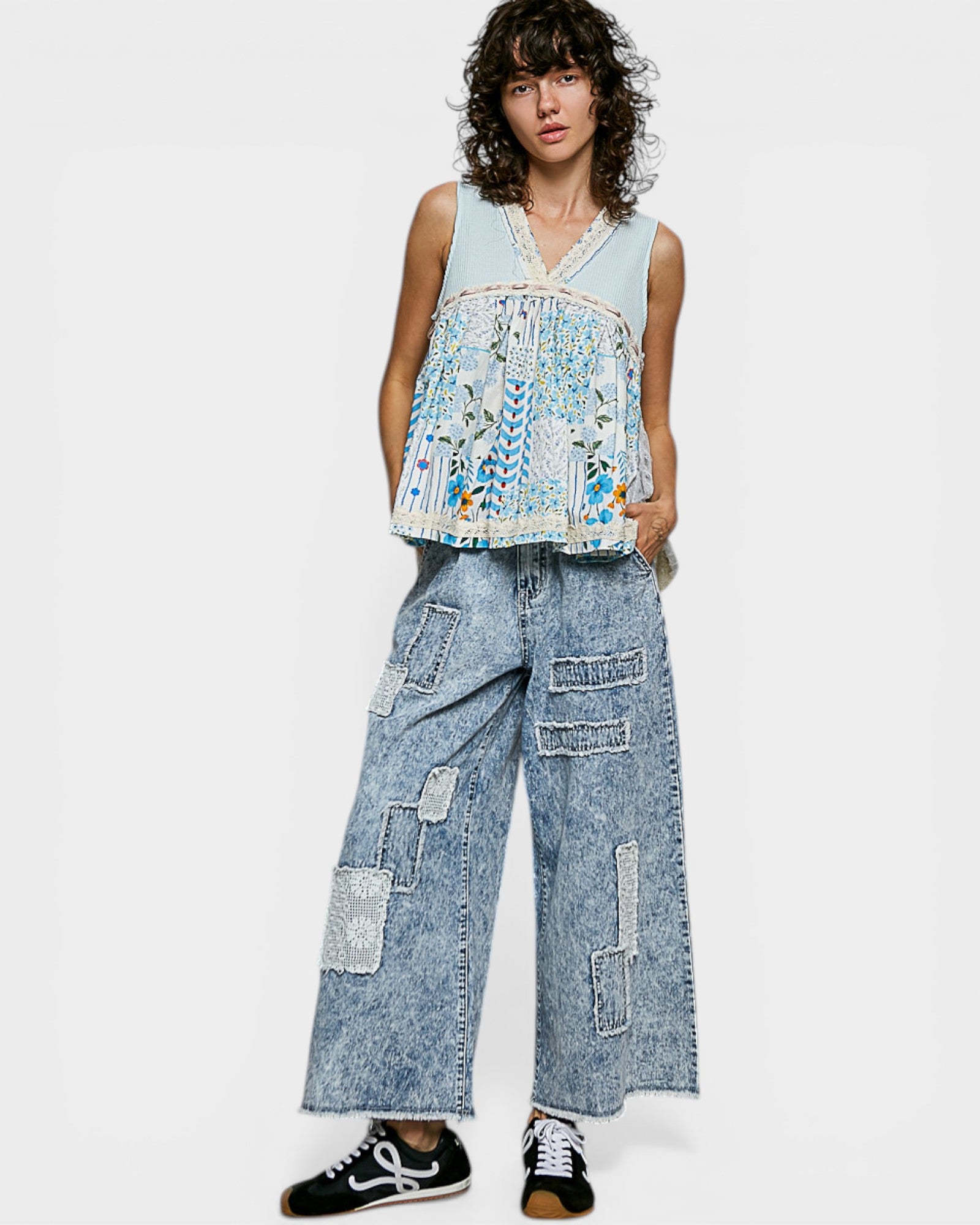 Person wearing a sleeveless top and wide-leg jeans with patchwork design on a white background