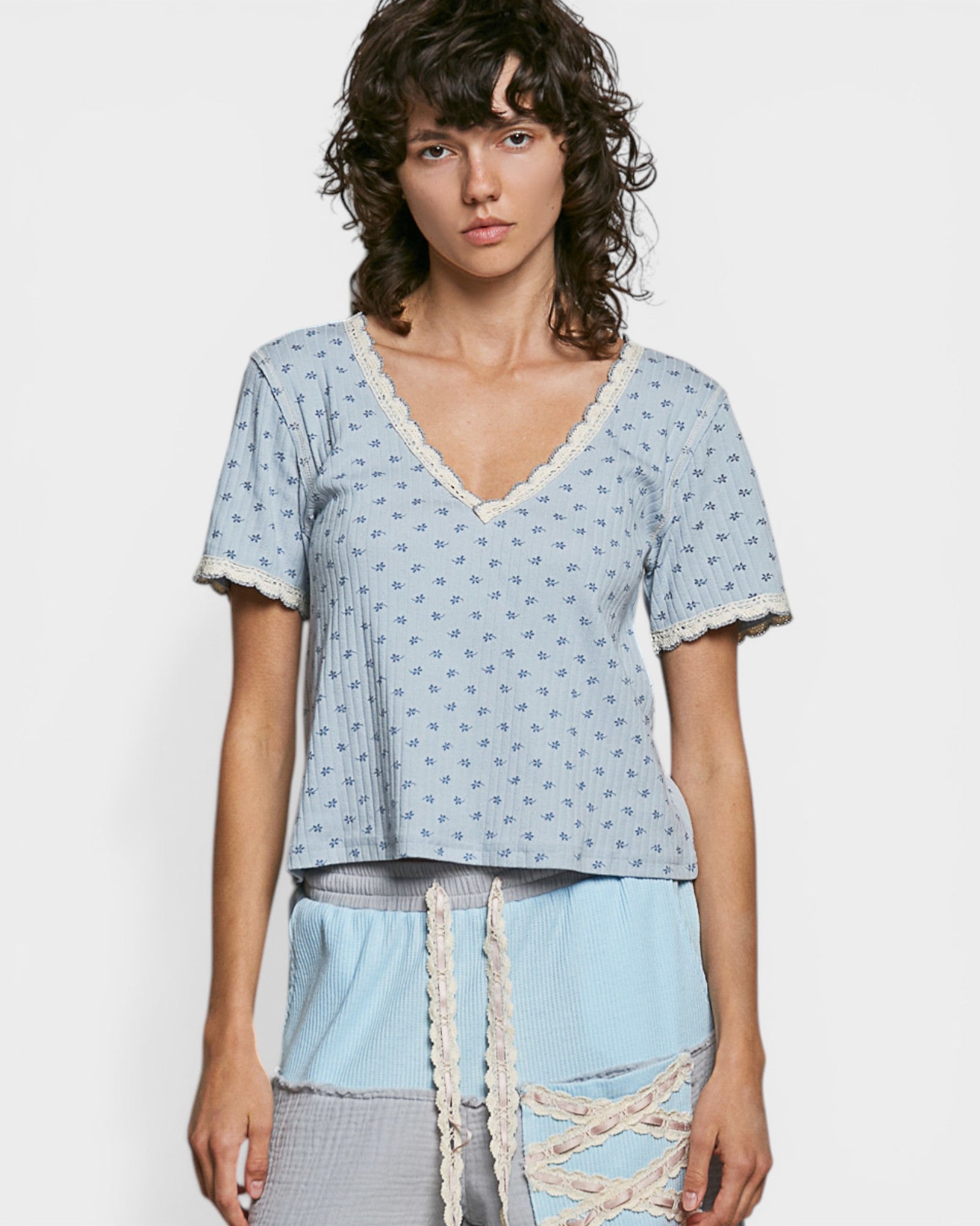 Woman wearing a light blue patterned top with lace details on a white background