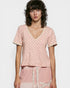 Woman wearing a pink patterned top and pants against a white background