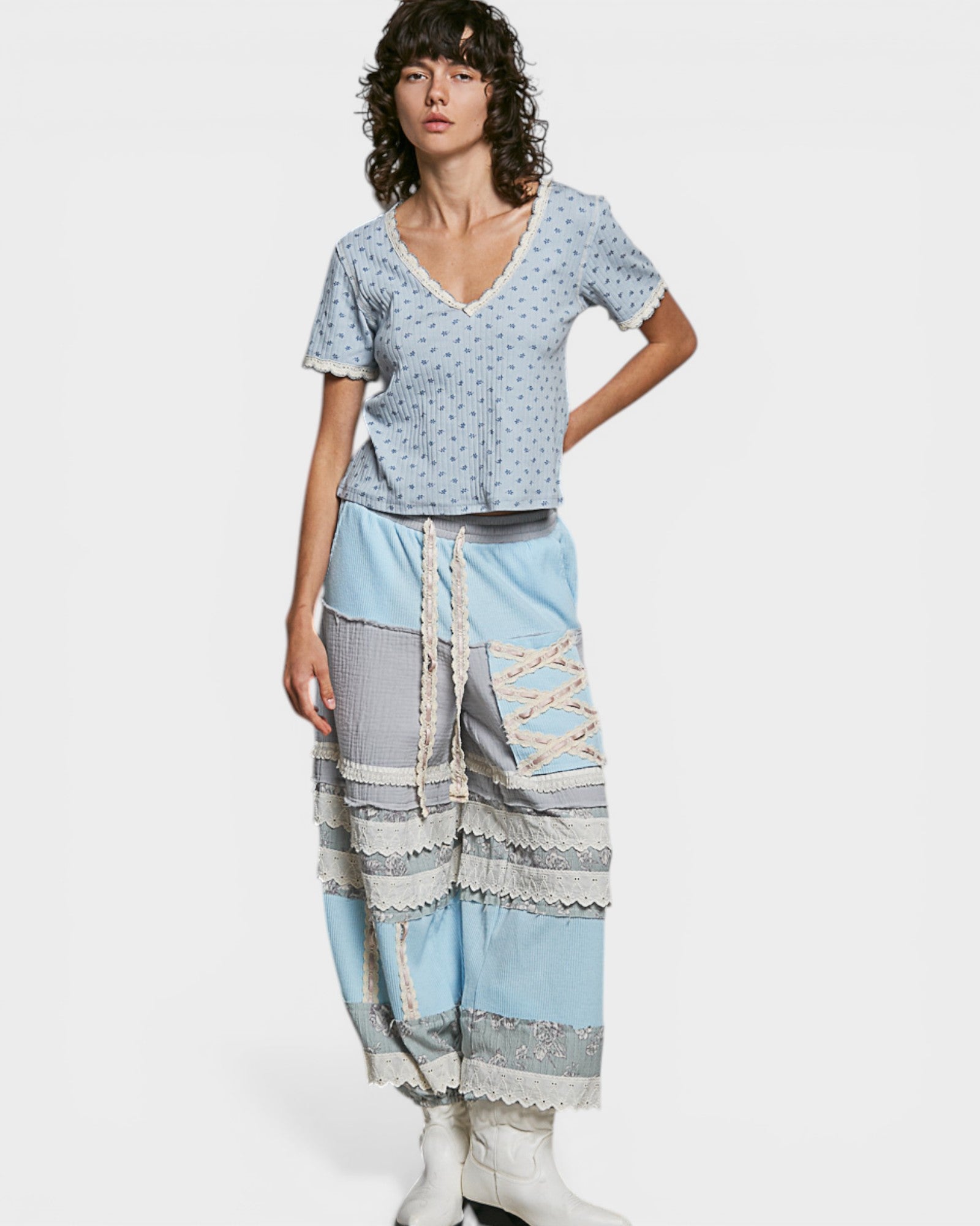 Woman wearing a light blue patterned top and layered pants on a white background