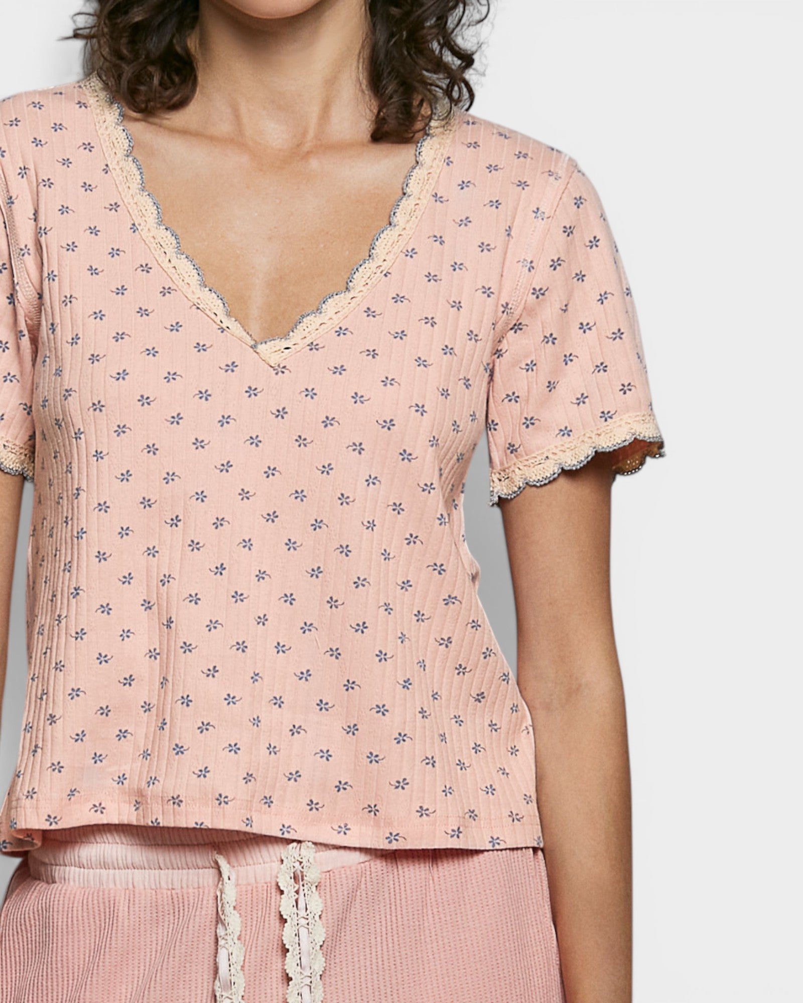 Woman wearing a pink floral top with lace trim on a plain background