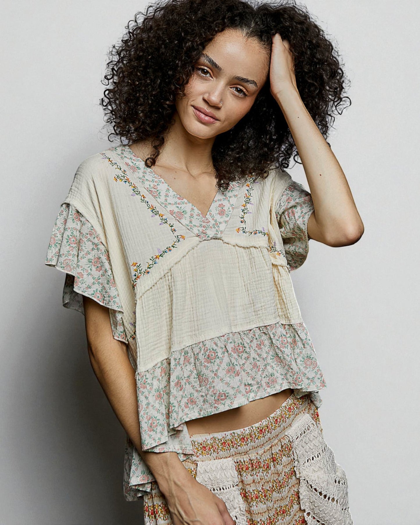 Woman wearing a layered, floral-patterned outfit against a plain background