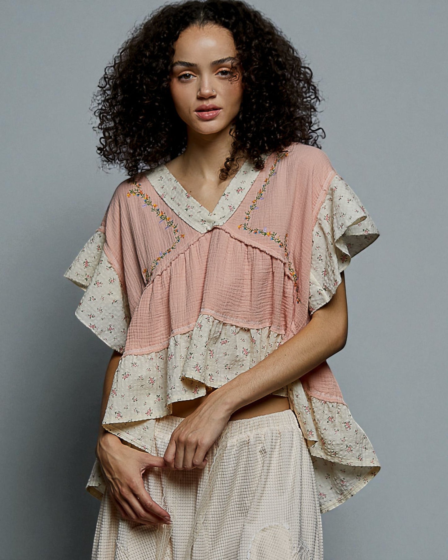 Woman wearing a layered outfit with a pink top and white skirt against a gray background