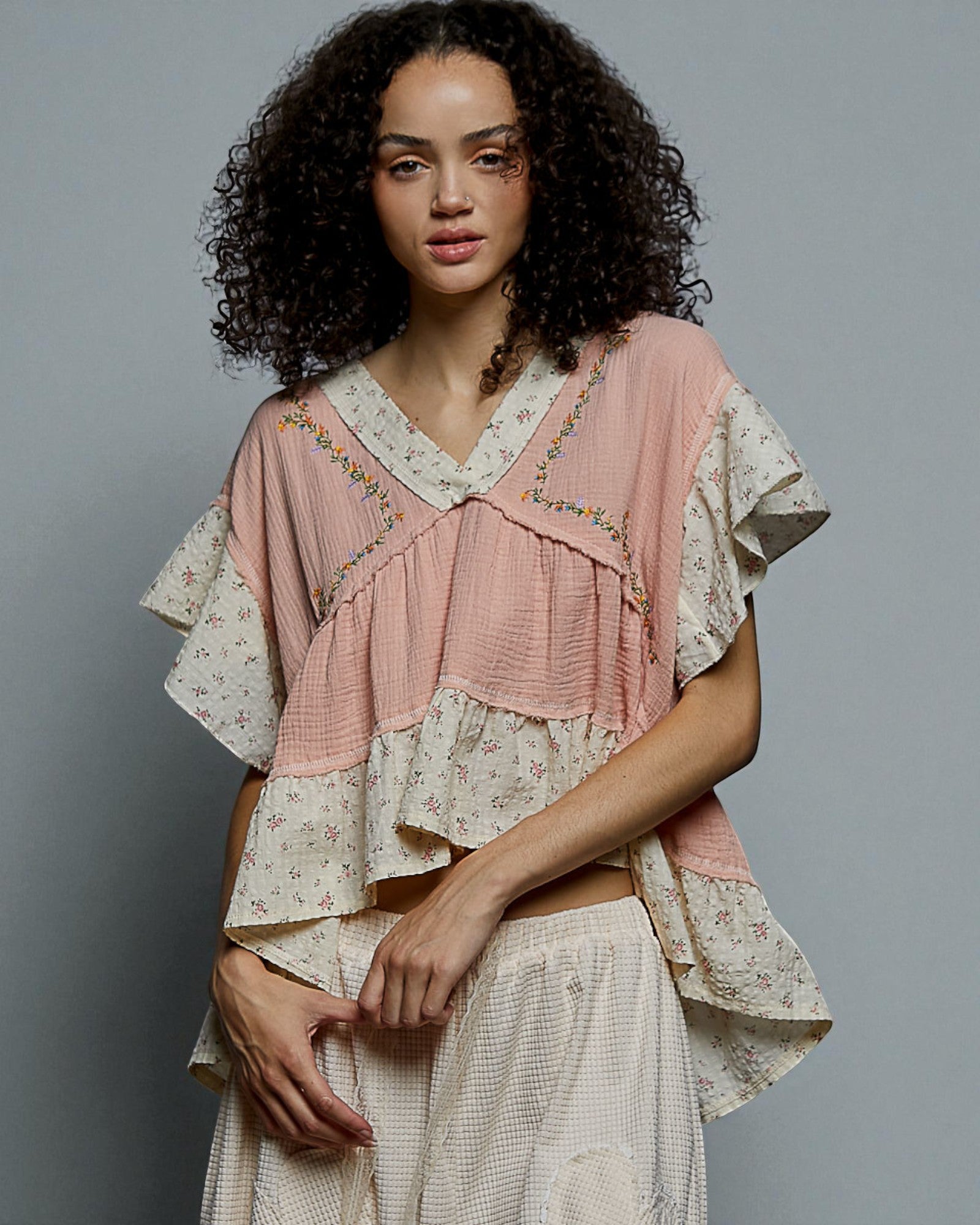 Woman wearing a layered outfit with a pink top and white skirt against a gray background