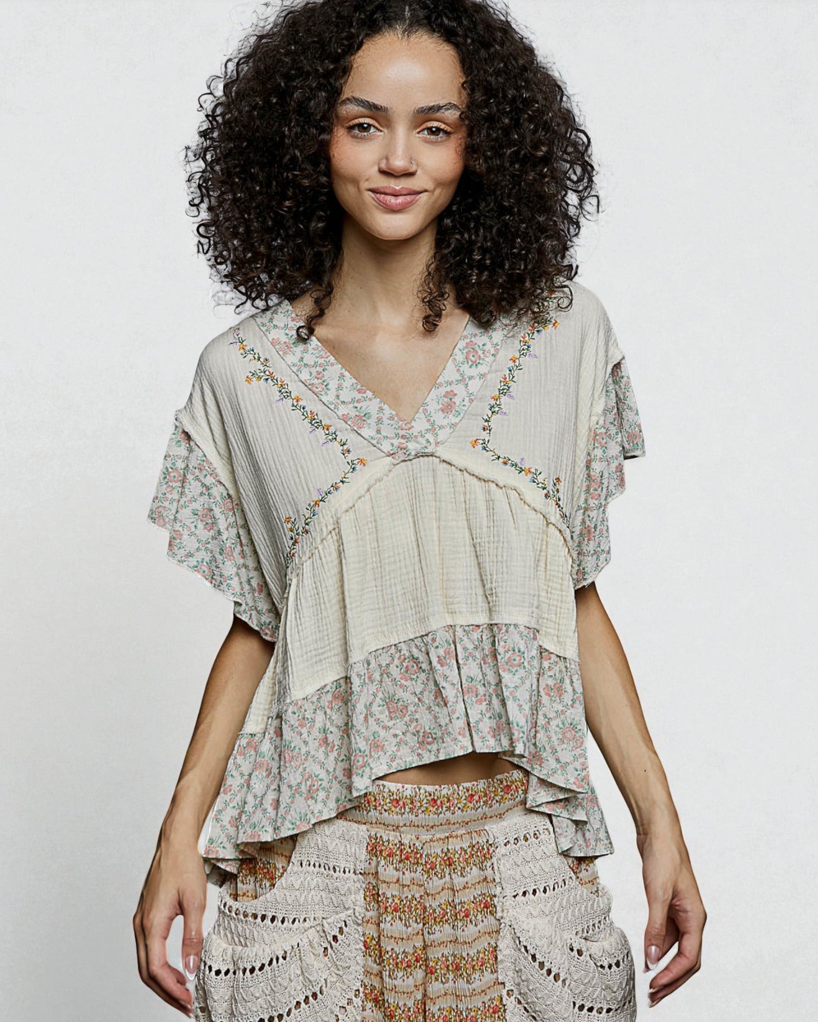 Woman wearing a layered, patterned top against a plain background