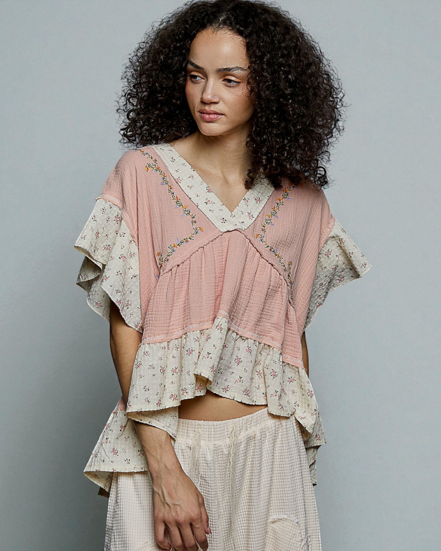 Woman wearing a layered, floral top and skirt against a plain background