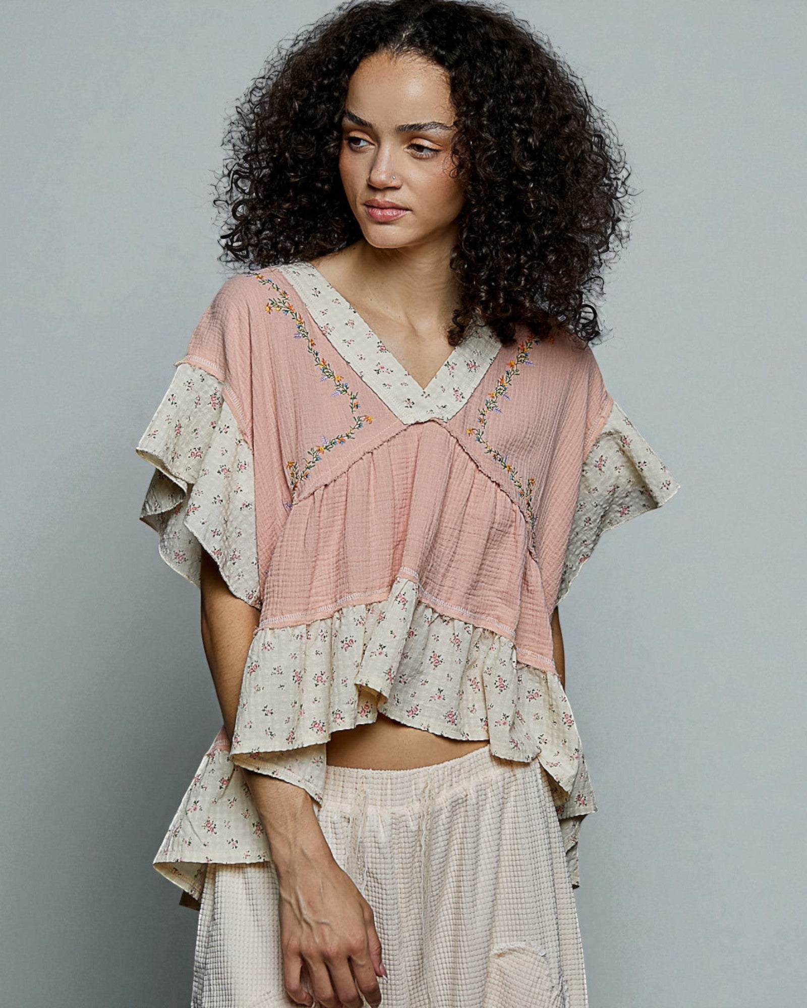 Woman wearing a layered, floral top and skirt against a plain background