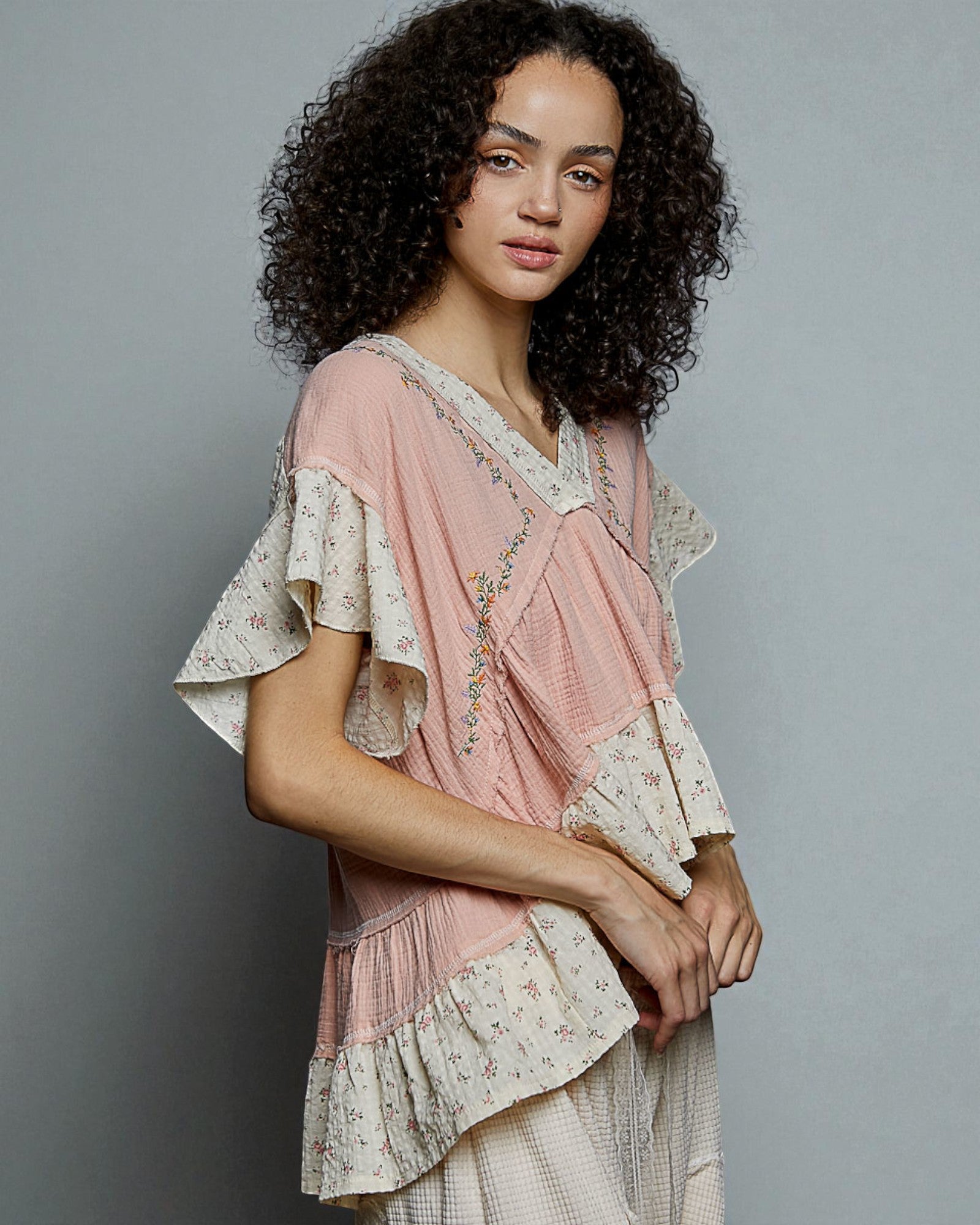 Woman wearing a pink and beige layered blouse with floral patterns on a gray background