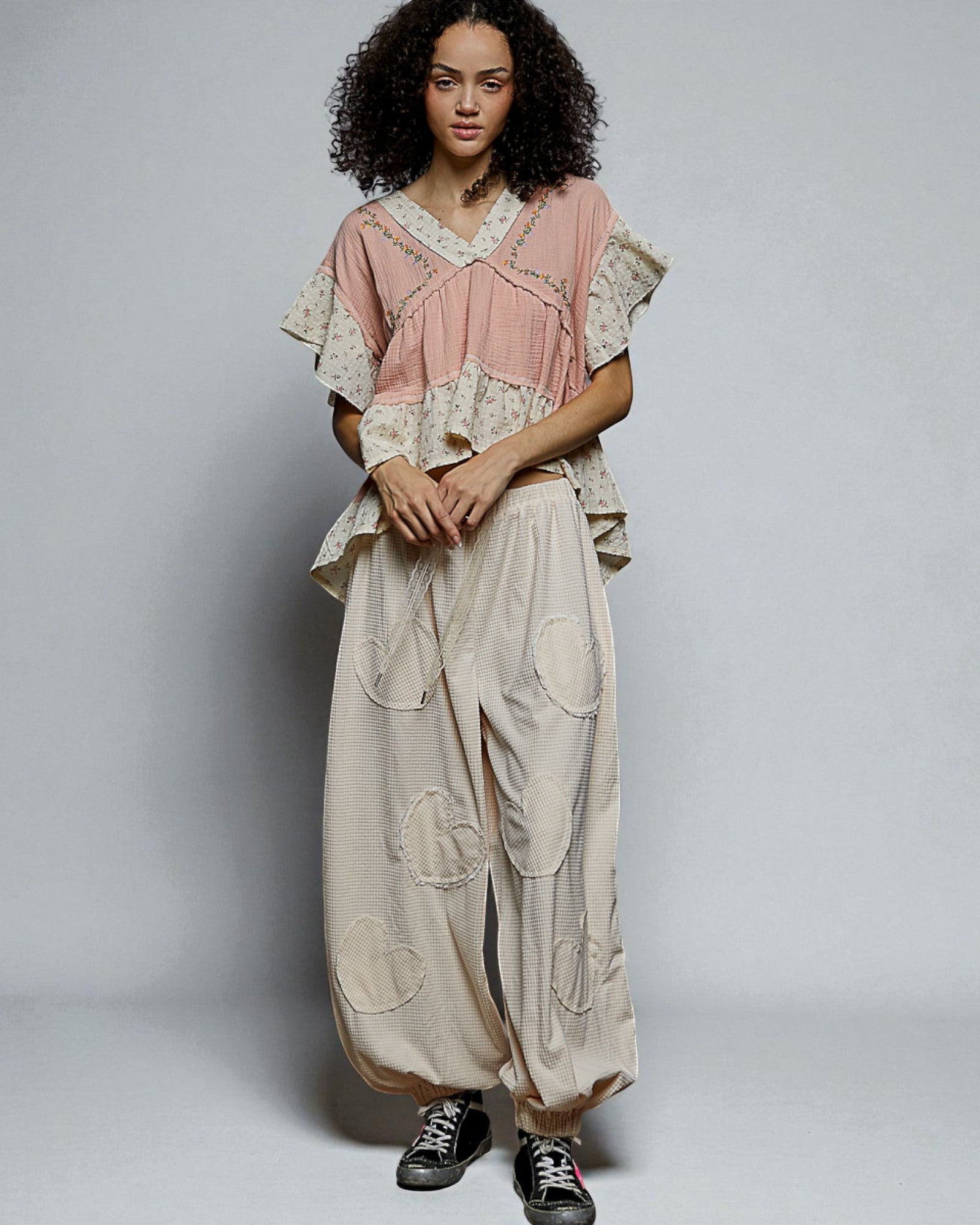 Woman wearing a layered outfit with a pink top and beige pants on a plain background