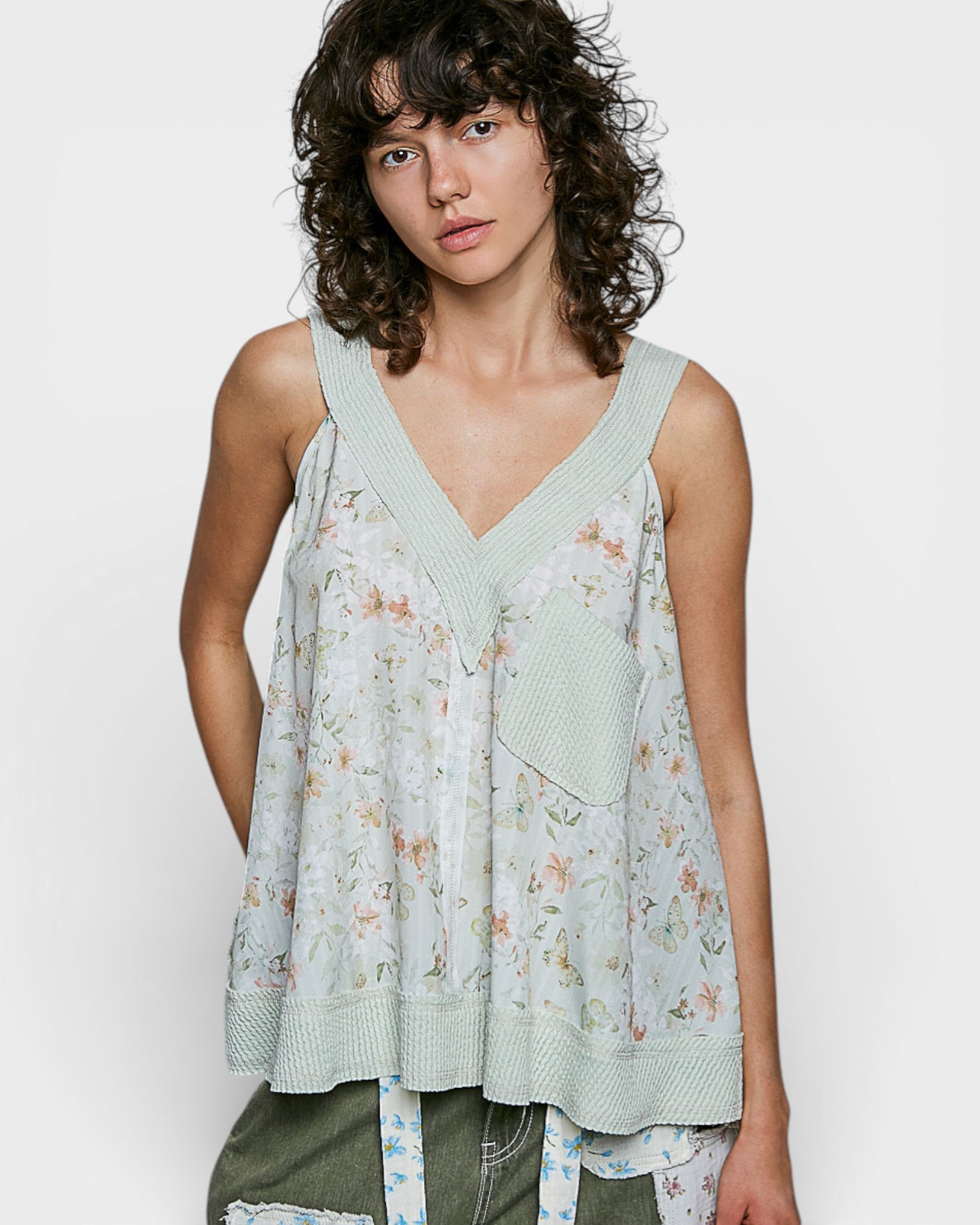 Woman wearing a light green floral sleeveless top against a white background