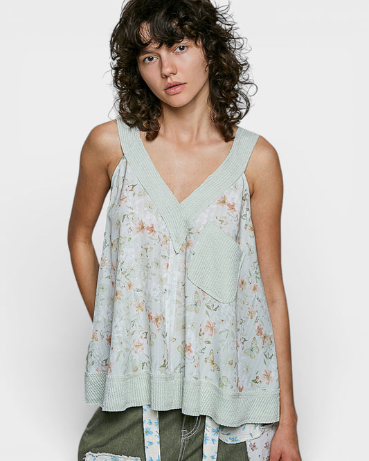Woman wearing a light green floral sleeveless top against a white background