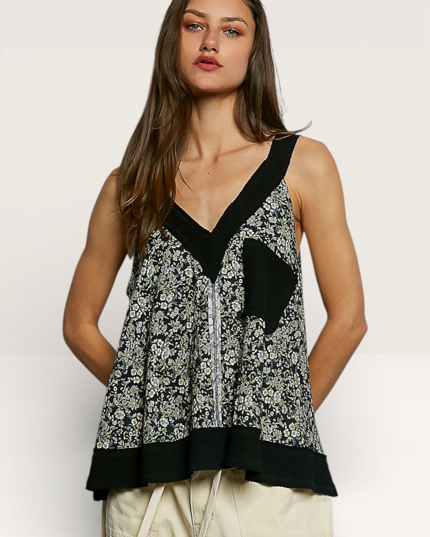 Woman wearing a black and white floral sleeveless top on a plain background