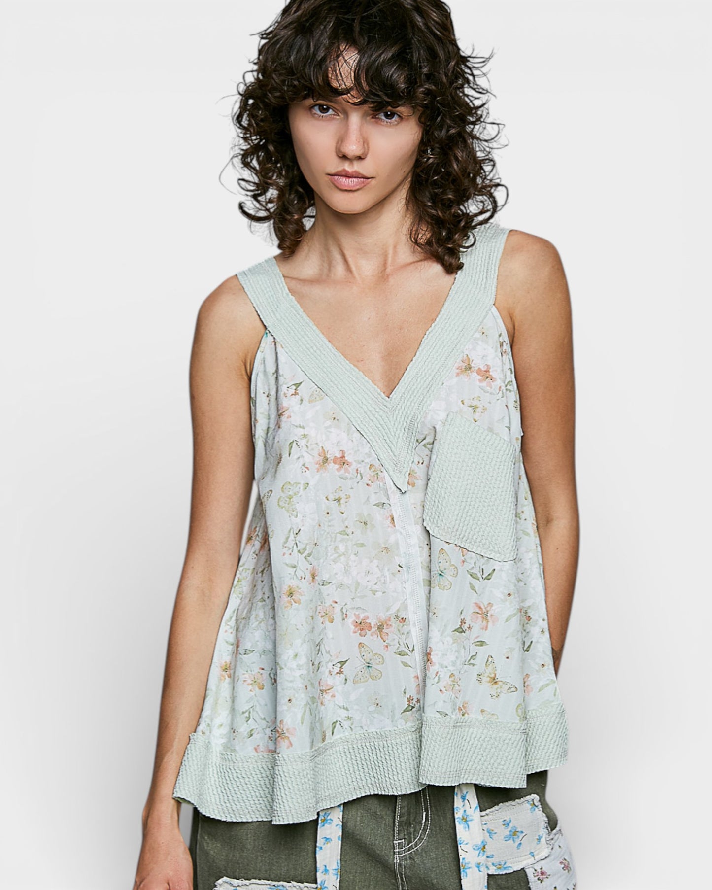 Woman wearing a light green floral sleeveless top against a white background