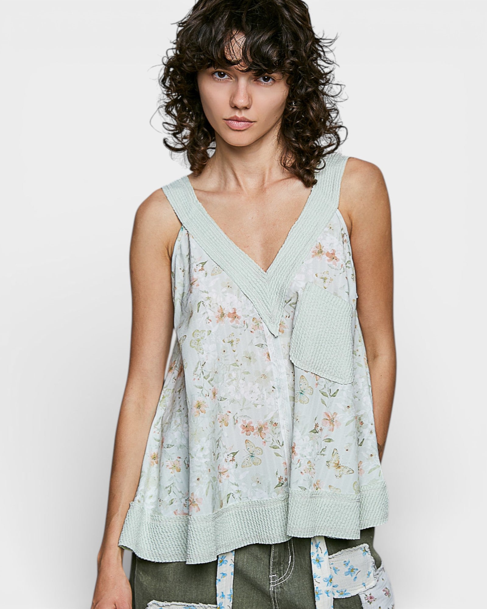 Woman wearing a light green floral sleeveless top against a white background
