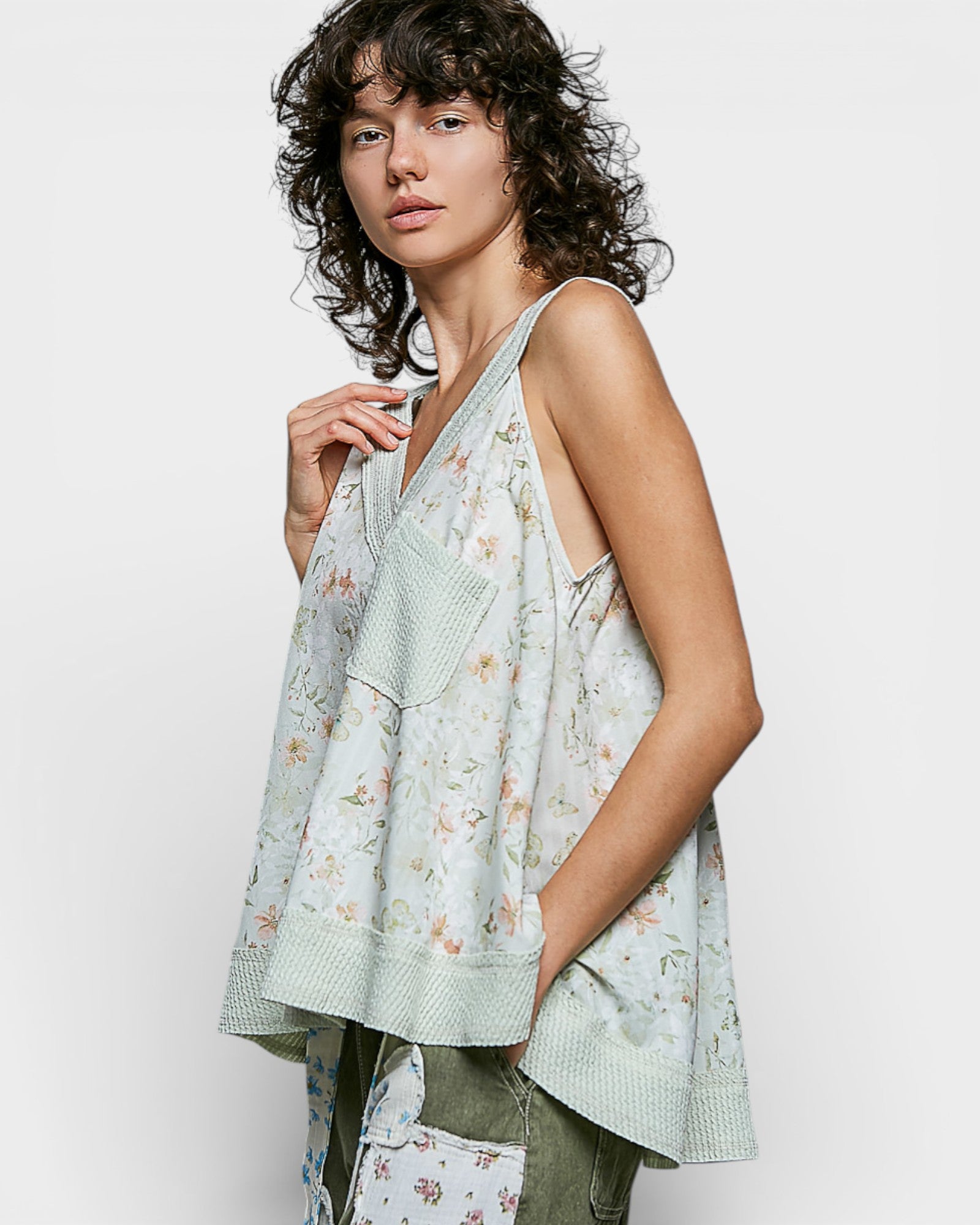 Woman wearing a light green floral sleeveless top against a white background