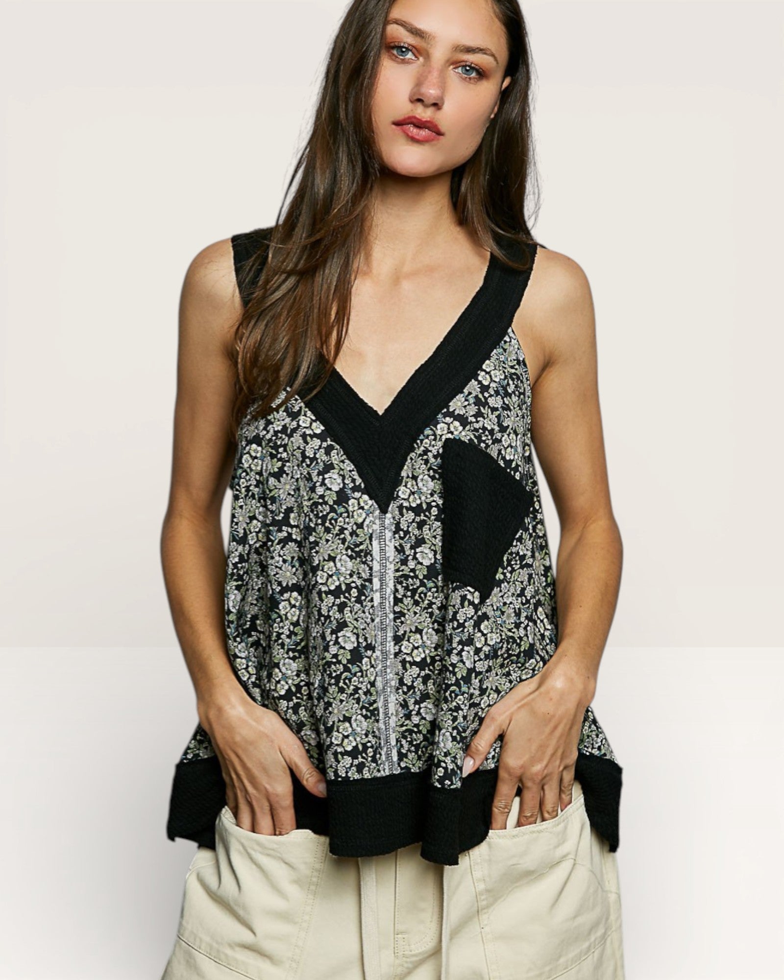 Woman wearing a sleeveless floral top with black accents on a plain background