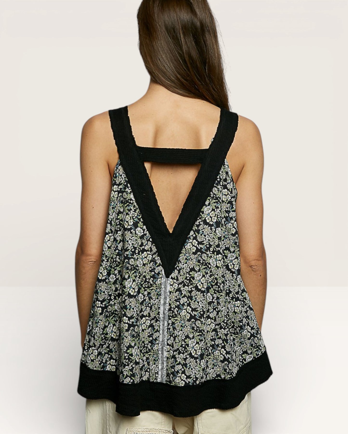 Woman wearing a floral tank top with black trim on a plain background