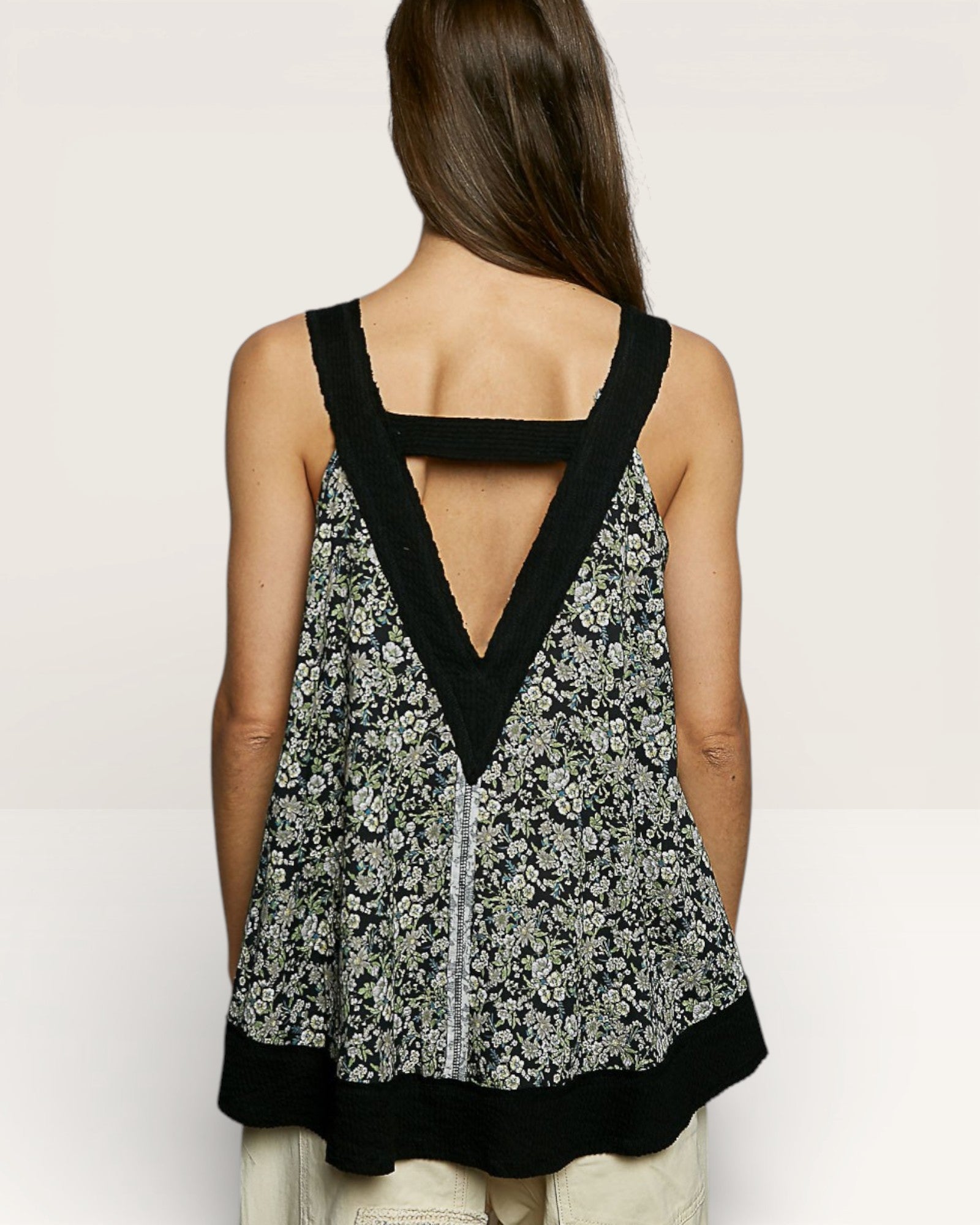 Woman wearing a floral tank top with black trim on a plain background