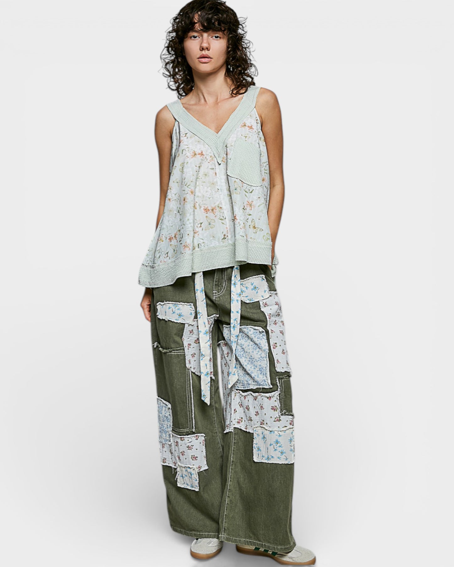 Person wearing a sleeveless top and patchwork pants on a white background