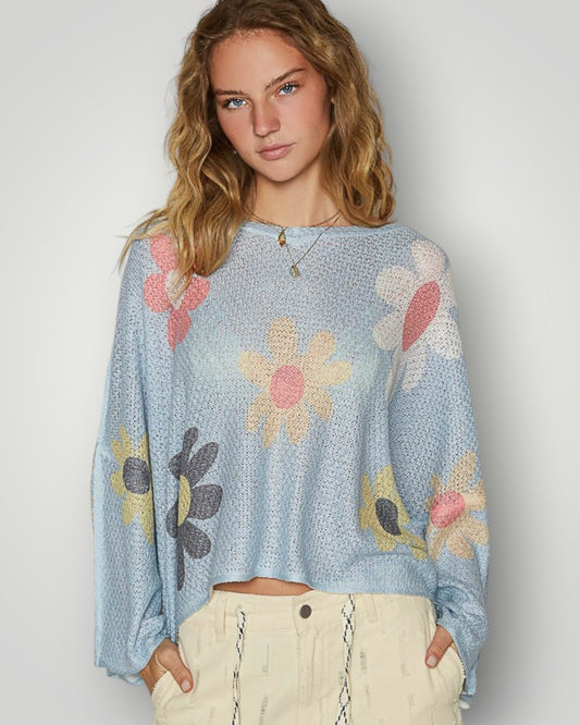 Woman wearing a light blue sweater with floral patterns on a plain background