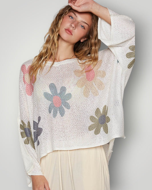 Woman wearing a white sweater with floral patterns on a plain background