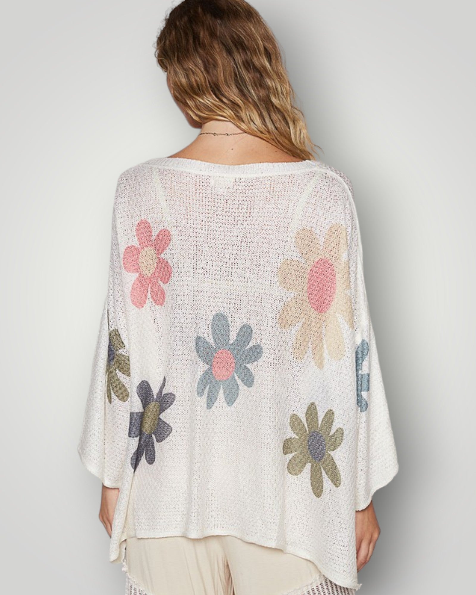 Woman wearing a white knit cardigan with colorful floral patterns on a plain background