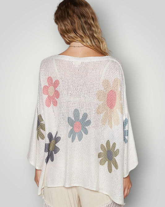 Woman wearing a white knit cardigan with colorful floral patterns on a plain background