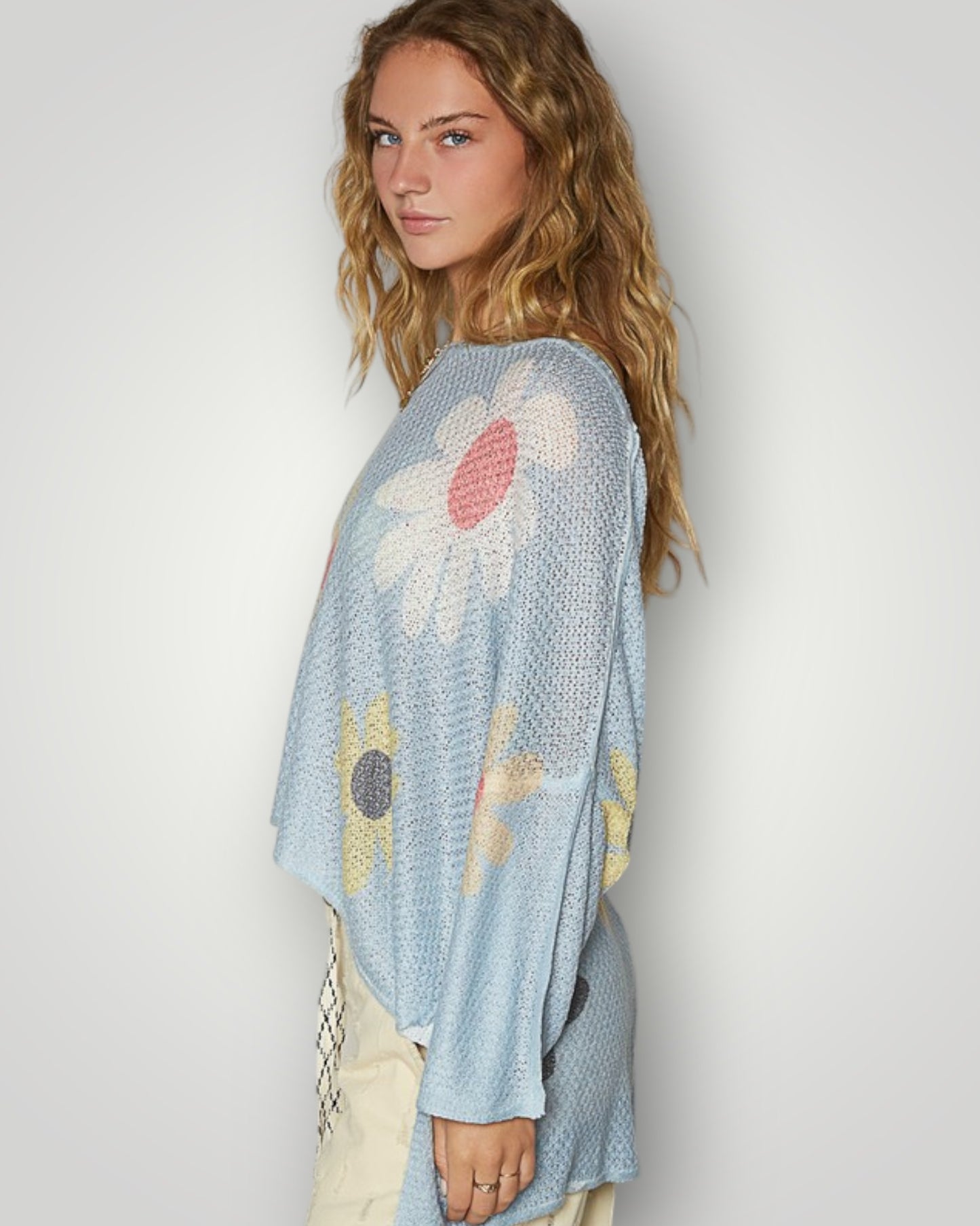 Woman wearing a light blue knit poncho with floral patterns against a white background